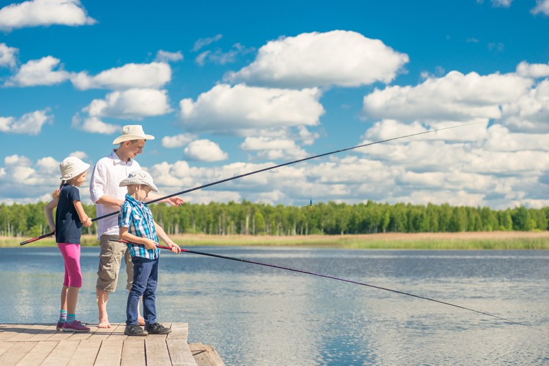 Ein Vater fischt mit seinen zwei Kindern am See