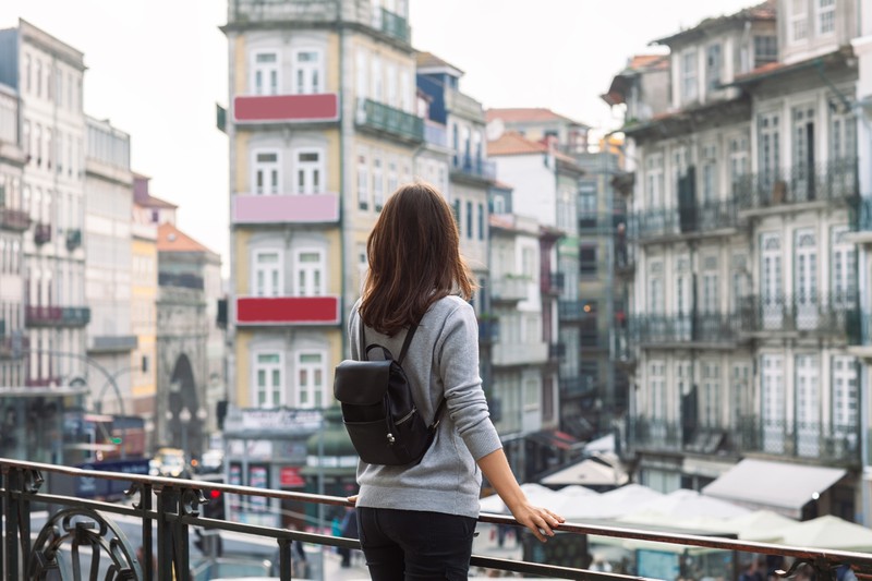 Zu sehen ist eine Frau, die in einer Stadt auf einem Balkon steht.