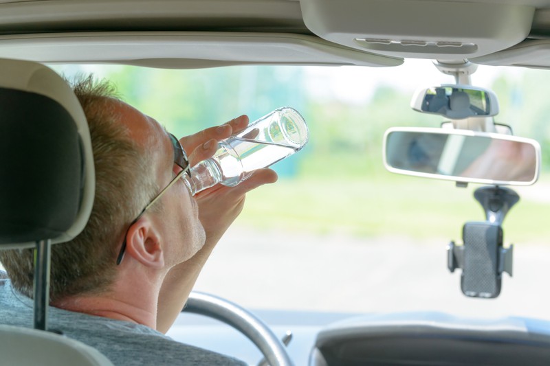 Ein Mann sitzt im Auto und trinkt aus einer Wasserflasche.
