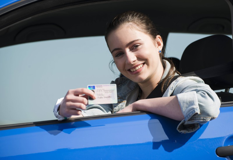 Zu sehen ist eine junge Frau, die ihren Führerschein in die Kamera hält.