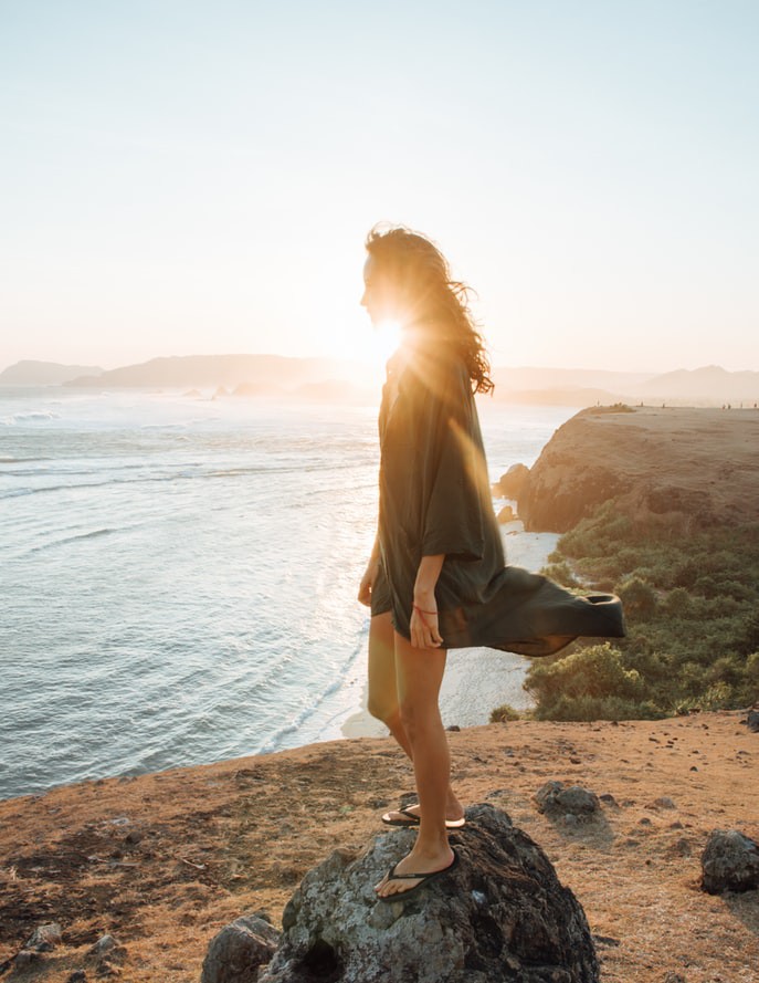 Frau, die auf Reisen auf einem Felsen am Meer steht