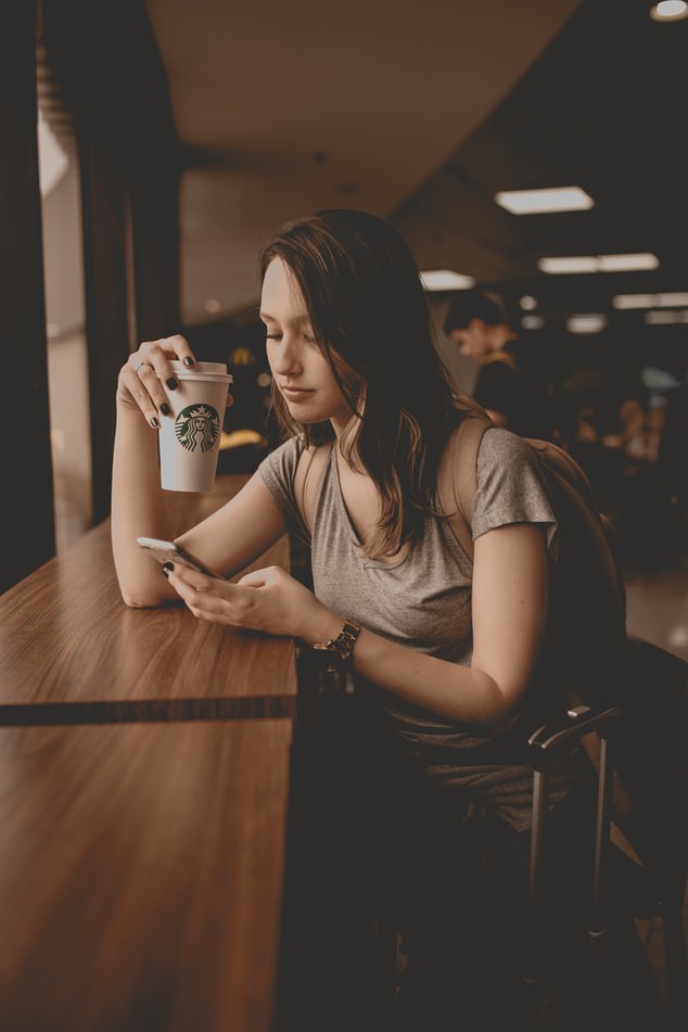 Frau, die allein in einem Café steht und auf ihr Handy schaut
