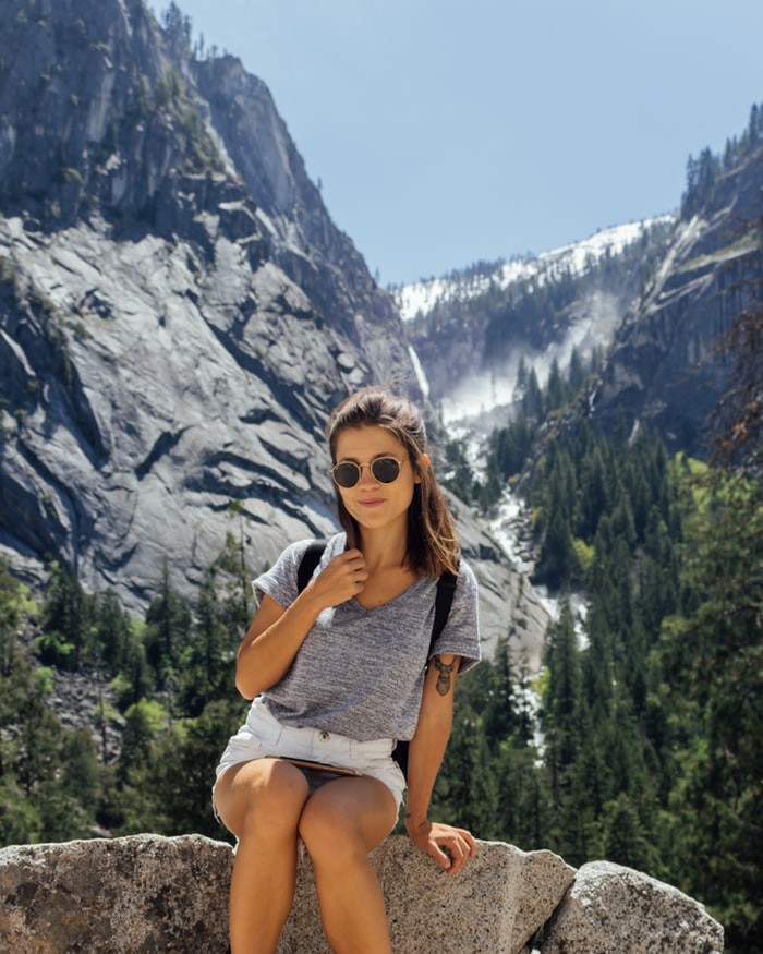 Vor einem Bergpanorama sitzt eine Reisende allein auf einem Stein