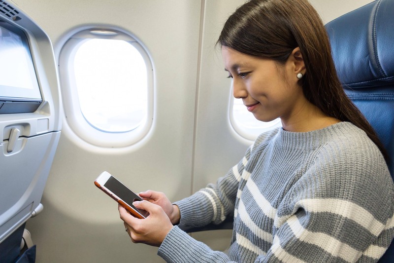 Man sieht eine Frau, die ihr Handy in den Flugmodus stellt, damit dem Mythos zufolge das Flugzeug nicht abstürzen kann