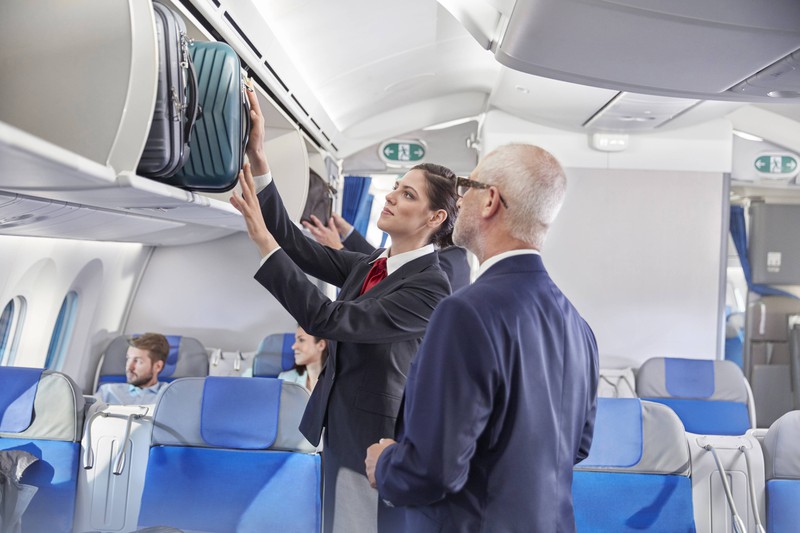 Man sieht eine Flugbegleiterin, die problemlos an die Gepäckfächer im Flugzeug gelangt