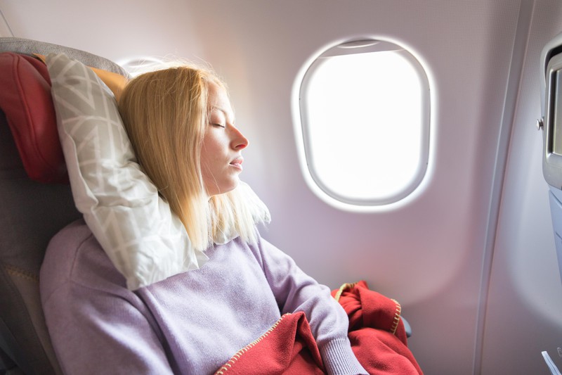 Eine schlafende Frau, die gemütlich mit viel Platz im Flugzeug sitzt.