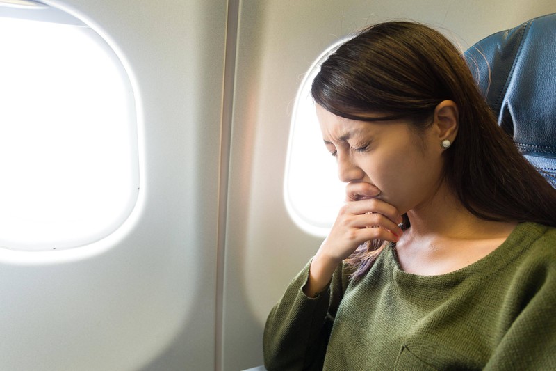 Einer Frau wird im Flugzeug schlecht: So geht es vielen Menschen mit Reiseübelkeit.