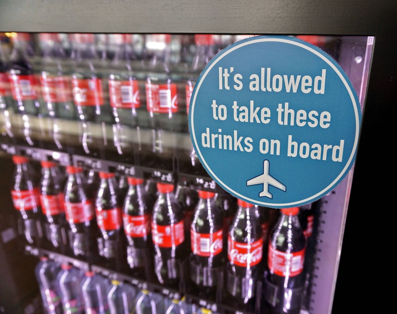 Es ist ein Snackautomat mit Getränken zu sehen, der zeigt, dass man jegliches Essen und Flüssigkeiten nach dem Sicherheits-Check ins Flugzeug mitnehmen darf