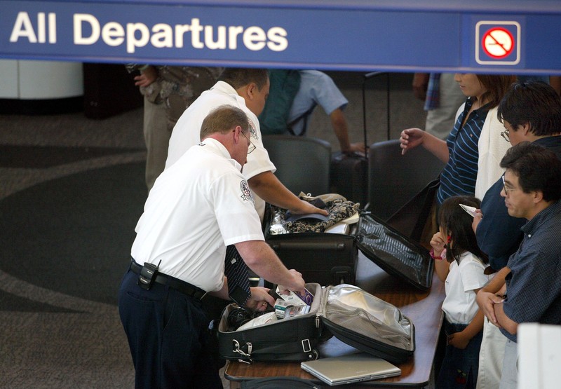 Männer durchsuchen Handgepäck am Flughafen am Security Check-in um vielleicht nach Flüssigkeiten und Essen zu kontrollieren