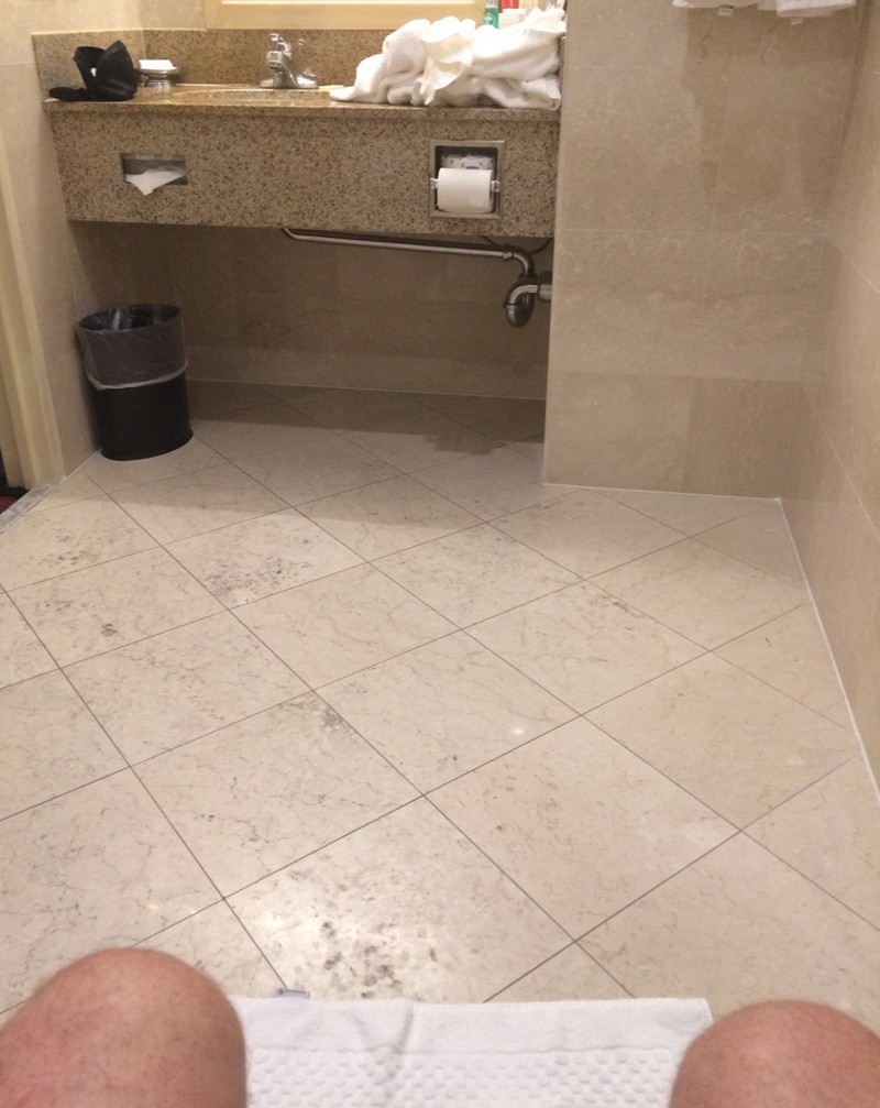 Ein Mann sitzt im Hotel  auf dem Klo, aber das Toilettenpapier befindet sich viel zu weit weg
