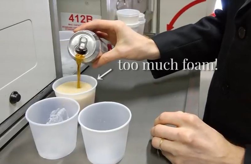 Ein Steward schenkt Cola in einen Becher im Flugzeug ein.